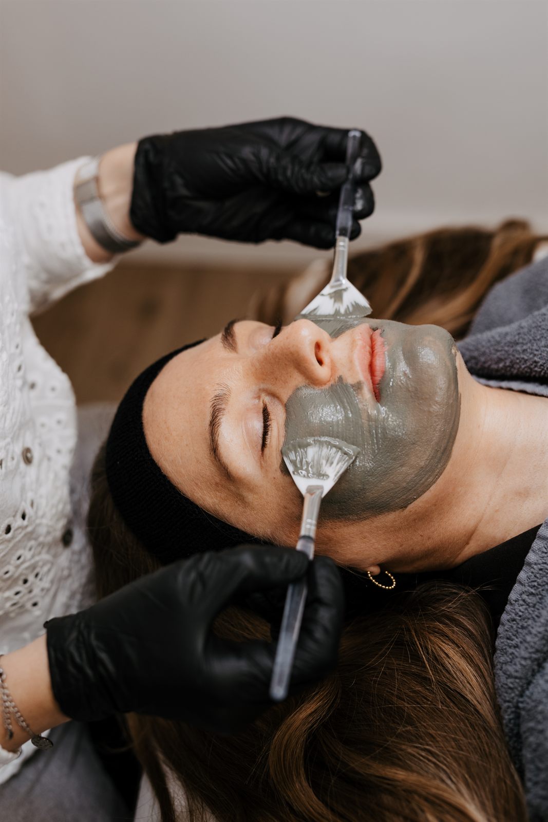 Graue Maske wird bei der Gesichtsbehandlung auf Wange und Kinn aufgetragen