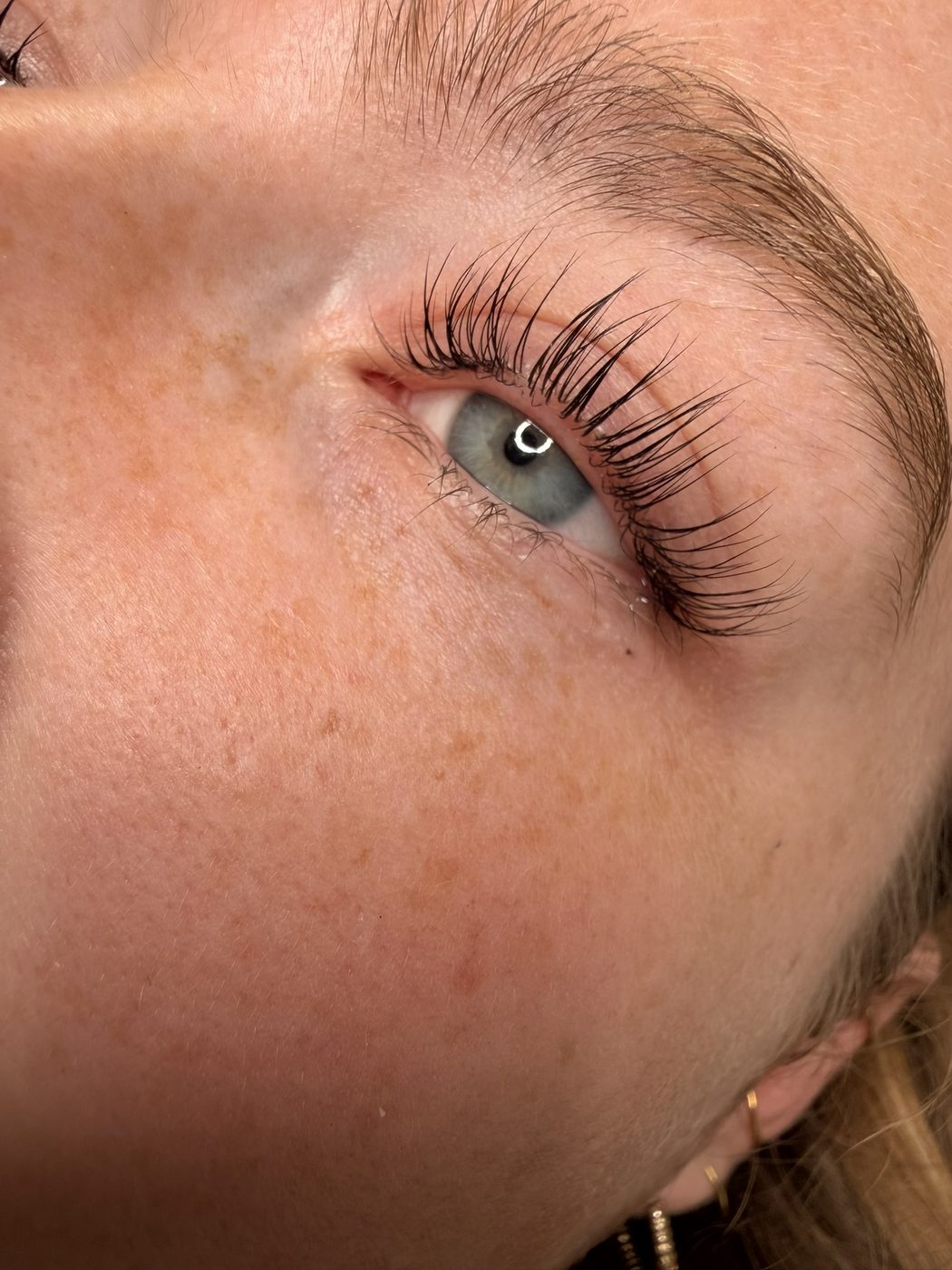 Blaugraues Auge mit Sommersprossen und goldenen Creolen nach dem Korean Wimpern Lifting
